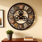 Decorative wall clock with gear design on a beige wall, below a framed picture and books on a wooden shelf.